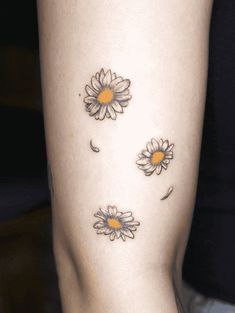 a woman's leg with three daisies on the lower part of her thigh