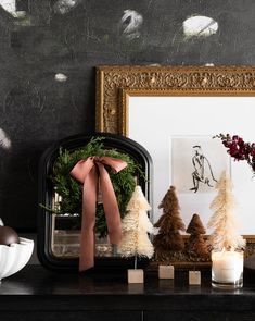 a mantle with christmas decorations, candles and a framed photograph on it in front of a wallpapered background