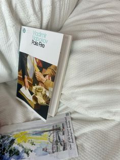 a book sitting on top of a white bed next to a person's hand