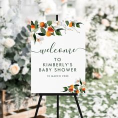 a welcome sign for a baby shower with oranges and greenery on the background