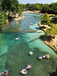 people are in boats on the water near some trees and other small boats that are floating down the river