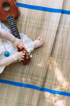 a small child is playing with a ukulele on the ground next to a guitar