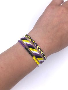 a person's hand with two bracelets on their wrist and one is wearing a yellow, purple, and white chevron