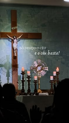 people sitting in front of a cross with candles on the ground and an image of jesus above it