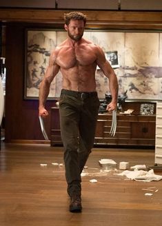 a shirtless man walking through a living room holding a wolverine stick in his right hand