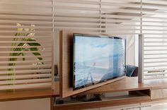 a flat screen tv sitting on top of a wooden shelf next to a window covered in blinds