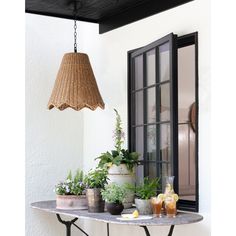 a table topped with potted plants next to an open window and a hanging lamp