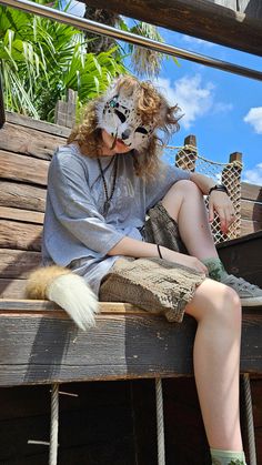 a person sitting on a wooden bench with a cat mask over their face and legs