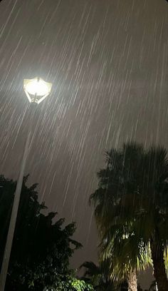 the street light is shining brightly in the night sky with rain falling down on it