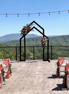 an outdoor ceremony set up with orange sashes and floral arrangements on the top of a hill