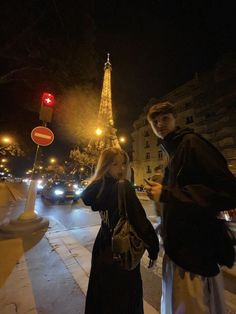 a man and woman standing on the sidewalk in front of the eiffel tower