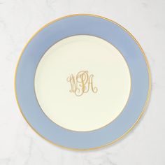 a blue and white plate with a monogrammed initial on the side, sitting on a marble surface