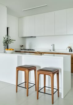 two stools sit in front of an island with white countertops and cabinets,