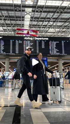 two men are walking through an airport with their suitcases and one man is holding his hand out