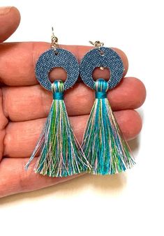 a pair of blue and green tasselled earrings on a person's hand