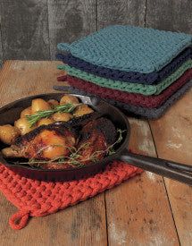 four crocheted dishcloths are sitting on a wooden table next to a cast iron skillet