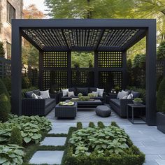 an outdoor living area with black furniture and green plants in the center, surrounded by hedges