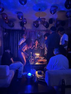 a group of people standing around a table with a cake on it in the middle of a room