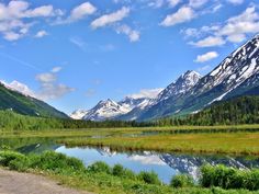 the mountains are covered in snow and green grass near a small lake with water running through it