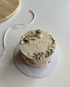 a white cake sitting on top of a table next to a wooden plate with a purple ribbon