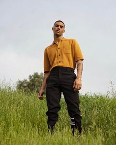 a man standing in the middle of a field wearing black pants and an orange shirt