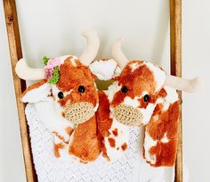 two brown and white cow stuffed animals sitting on top of a blanket in a chair