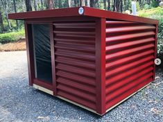 a small red shed sitting on top of a gravel road in front of some trees