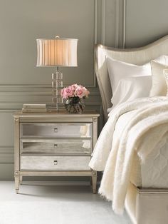 a white bed sitting next to a nightstand with flowers on it