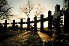 the sun is setting behind a large cross in a park with flowers and trees on either side