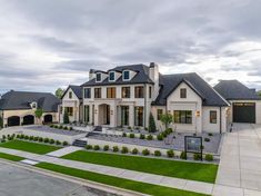 a large white house with lots of windows and grass in front of it on a cloudy day