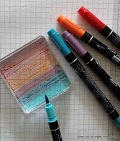 four markers and three pens on top of a piece of paper with squares in the background