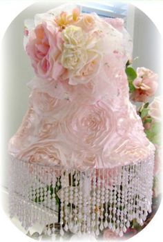 a pink and white wedding cake with flowers on it's tiered base, surrounded by pearls