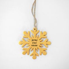 a gold snowflake ornament that says pray for snow