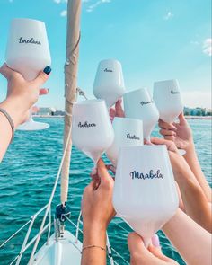 a group of people holding wine glasses over the top of a sailboat in the ocean