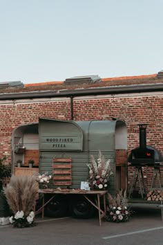 an old fashioned food truck parked in front of a brick building with flowers on it