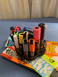 several pens and markers in a holder on a table with blue sheets behind it,