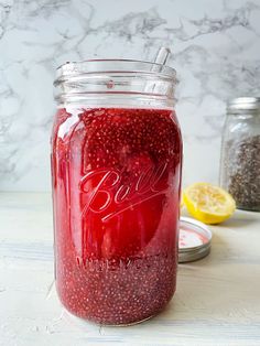 a jar filled with red liquid sitting on top of a table next to lemons