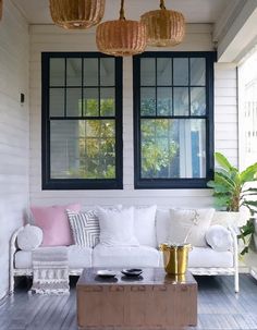 a white couch sitting on top of a wooden floor next to two large windows in a living room