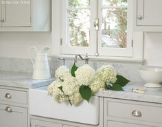 some white flowers are sitting on the sink in this clean and organized kitchen with marble countertops