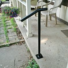 a metal hand rail sitting on the side of a sidewalk next to a table and chairs