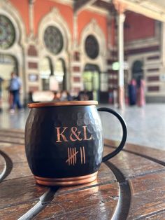 a black and copper coffee mug sitting on top of a wooden table in front of a building