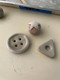 three ceramic objects sitting on top of a white table next to a metal object with holes in it