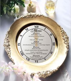 a gold plate with roman numerals on it next to some flowers and glasses