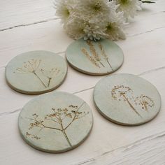 four ceramic coasters with flowers on them sitting on a table next to some white flowers