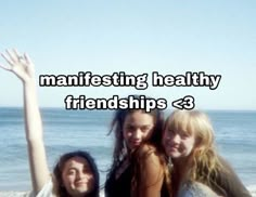 three girls are standing on the beach with their arms in the air and one girl is raising her hand