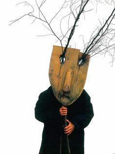 a person wearing a mask with branches on their head and holding an umbrella in front of them