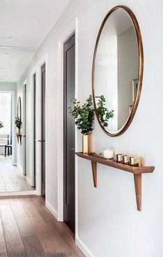 a hallway with white walls and wooden flooring has a large round mirror on the wall