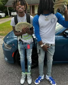 two young men standing next to each other in front of a blue car holding money