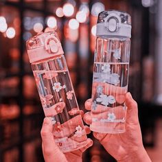 two people holding up clear water bottles with flowers on them