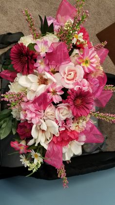 a bouquet of pink and white flowers sitting on top of a blue table next to a black bag